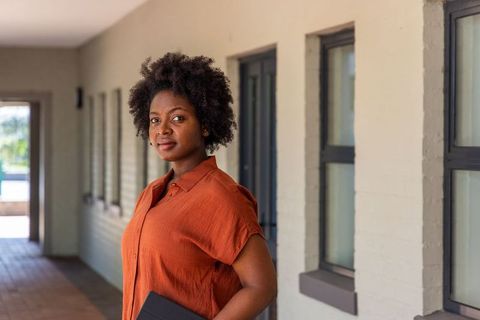 African american professional woman standing in corridor holding laptop sleeve confident