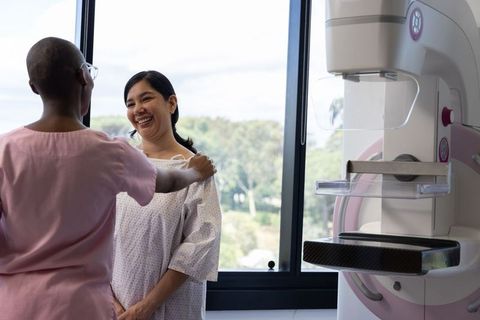 Radiology technician guiding asian woman during mammogram procedure in clinic