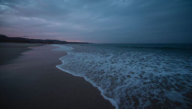 Twilight Surf Caressing Wet Sand Along Rocky Headlands Under Moody Lavender Cloudscape
