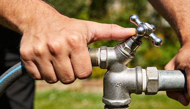 Hands connecting garden hose to outdoor spigot and metal faucet close-up for diy watering tasks