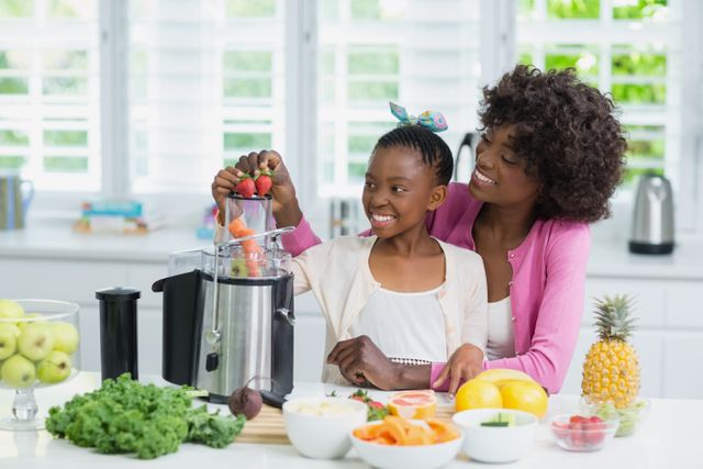 Mother and daughter are seen preparing a strawberry smoothie together in a bright, modern kitchen. The scene is filled with fresh fruits and vegetables, indicating a healthy lifestyle. This image is perfect for use in articles or advertisements related to family bonding, healthy eating, nutrition, and home cooking.
