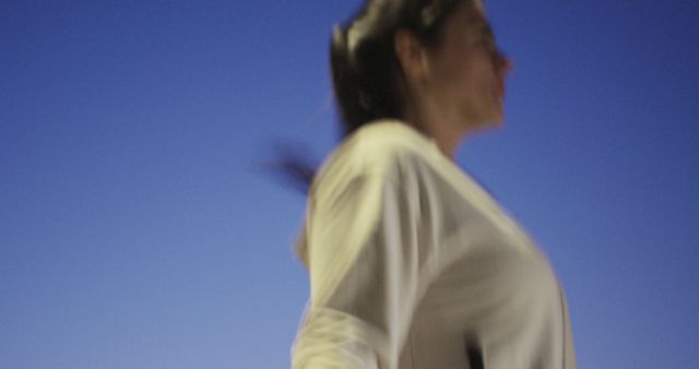 Blurred motion of the woman running at dusk, capturing the dynamic effort and movement involved. Perfect for use in articles or advertisements related to fitness, active lifestyle, evening workouts, or motivation.