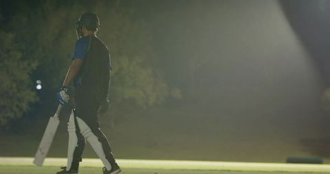 Teenage cricketer walking on night pitch tapping bat with teammate and resuming innings