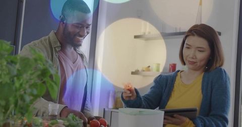 Smiling multicultural couple preparing healthy meal with tablet and countertop appliance in kitchen