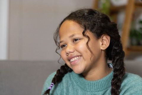 Smiling girl with braided pigtails wearing teal sweater on cozy living room sofa