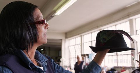 Happy Senior Woman Inspecting Hat in Workshop
