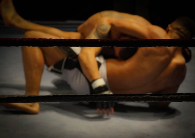 Two MMA fighters are engaged in a grappling battle inside the ring. Great for promoting martial arts competitions, physical fitness training programs, or sports events. Can be used in articles about mixed martial arts, wrestling techniques, or athletic contests.