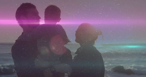 Parents holding baby on rocky shore at dusk with magenta lens flare and starry overlay