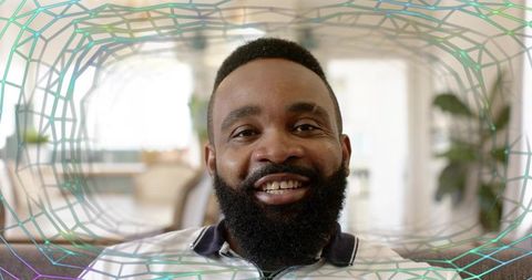 Smiling bearded man sitting on sofa in bright living room with polygonal graphic overlay