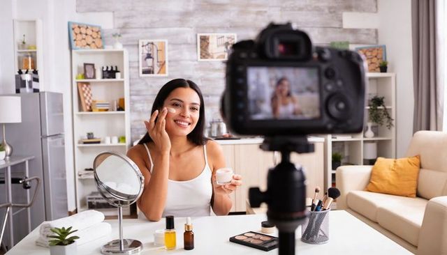 Hispanic beauty influencer applying skincare cream filming content in bright home studio