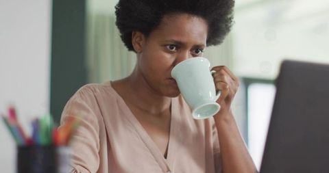 Focused Woman Drinking Coffee While Working on Laptop at Home Office