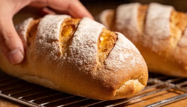 Hands lifting floured artisan loaf from metal cooling rack, closeup bread crust texture