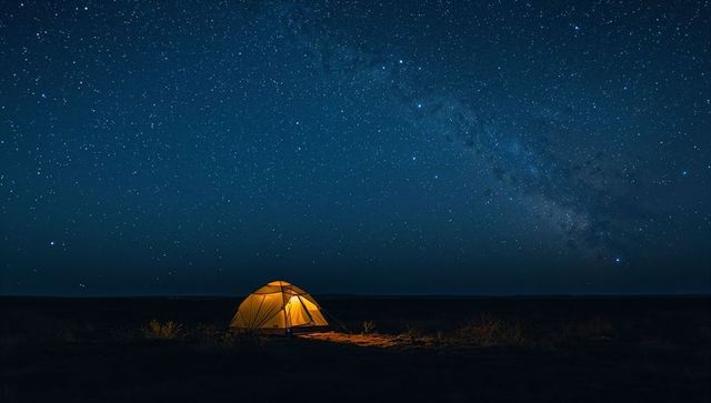 Glowing camp tent under milky way on open plain at night, starry sky and solitary landscape