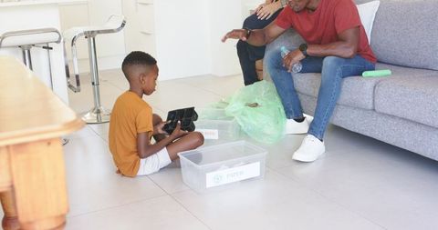 Child sorting recyclables with father in modern living room teaching home recycling