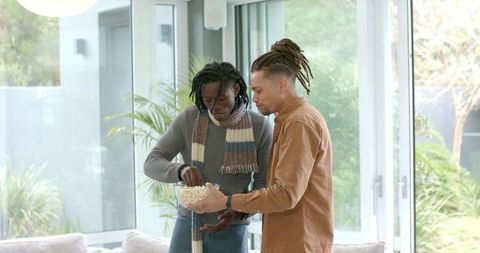 Mid-adult diverse friends sharing popcorn in sunlit modern living room