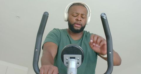 Man pedaling stationary bike wearing headphones checking console during home cardio
