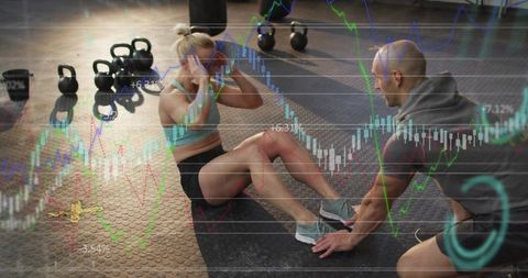 Coach holding feet while female trainee performing sit-ups in gym with kettlebells and chart overlay