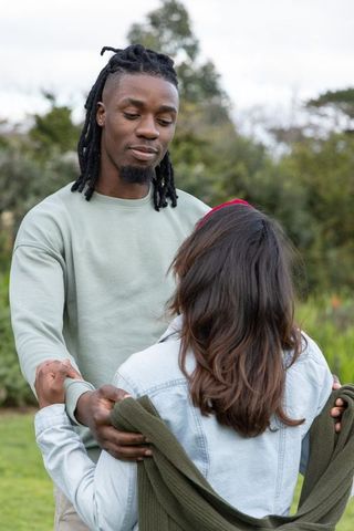 African american man wrapping green sweater around partner in tender romantic park moment