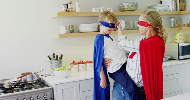 A young Caucasian boy and a middle-aged woman are playfully wearing superhero capes and masks in a kitchen, with copy space. Their imaginative play suggests a fun and bonding family activity.
