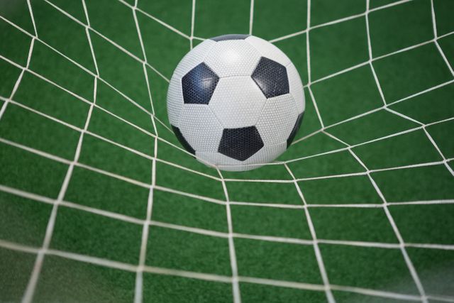 Soccer ball caught in goal net on artificial grass, ideal for sports-related content, advertisements, and articles about soccer or football. Perfect for illustrating concepts of scoring, victory, and competition.