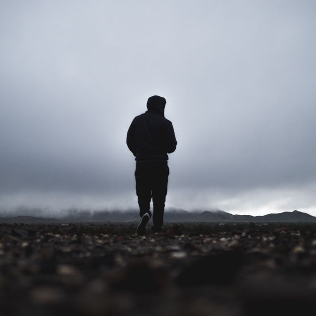 Person walking alone on rocky terrain under overcast skies, creating a moody and solitary atmosphere. Ideal for concepts of solitude, introspection, and contemplative moodiness. Can be used in articles and designs about feeling alone, self-reflection, mental health, or nature walks.