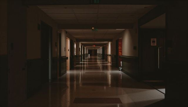 Moody empty hospital corridor leading to distant exit, reflective floor, closed doors