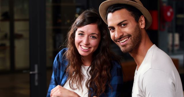 A young Caucasian woman and a young Middle Eastern man are smiling together, with copy space. Their cheerful expressions and casual attire suggest a relaxed social setting or a friendly encounter.
