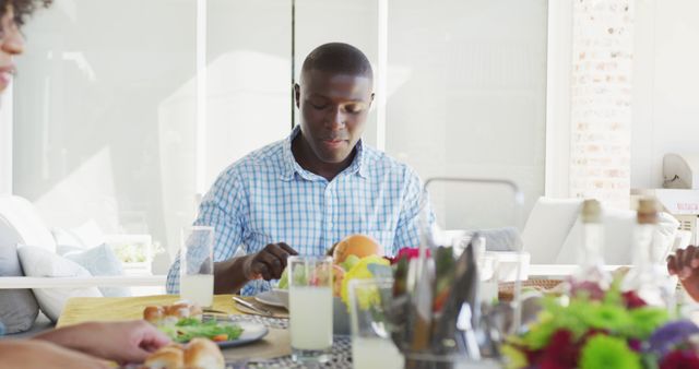Man dining at a brightly lit table, enjoying a healthy meal with salad and fresh juice. Surrounded by family members in a home setting. Ideal for illustrating family meals, healthy eating habits, breakfast routines, and lifestyle imagery.