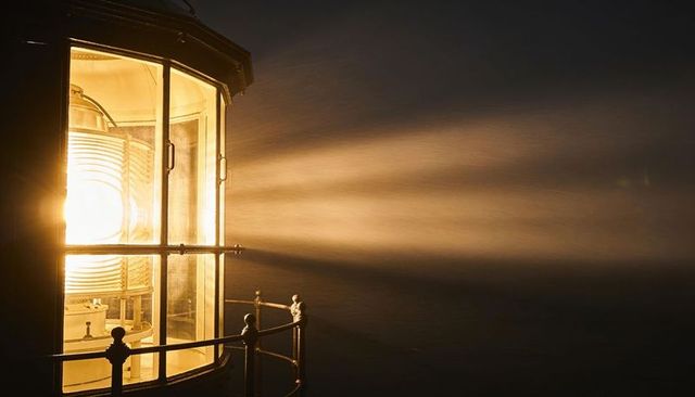 Golden beacon casting wide beam through foggy night over ocean