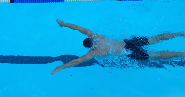 Overhead view of a male swimmer performing the butterfly stroke in a clear blue swimming pool. Ideal for illustrating fitness, sports training, and competitive swimming. Can be used in sports magazines, health and wellness articles, or athletic advertisements.