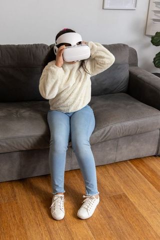 Asian girl wearing vr headset on sofa exploring virtual reality at home in cozy sweater