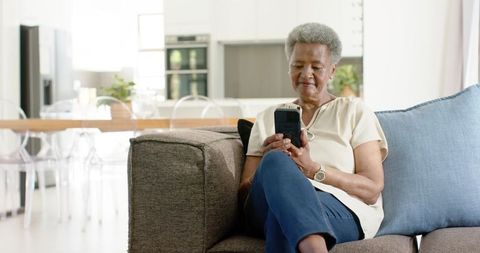 Senior african american woman relaxing on sofa using cordless phone in open-plan home