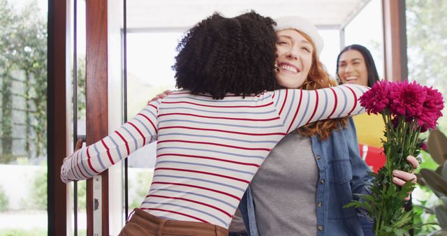 Friends sharing a warm hug at the doorway while one woman holds a bouquet of flowers. Perfect for depicting friendship, life events, and spirited reunion moments. Use for blogs, social media, greeting cards, and advertisements centered on relationships and joyful gatherings.