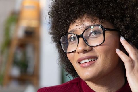 African american woman smiling touching ear wearing glasses in cozy home portrait