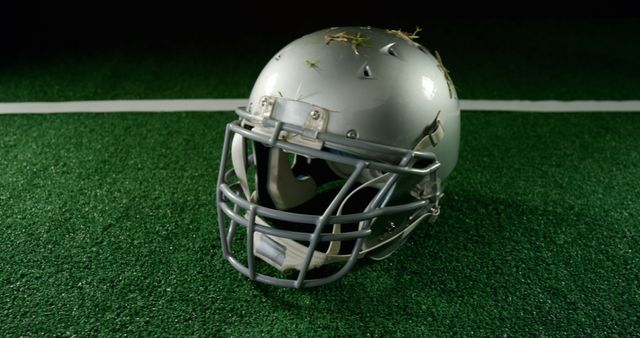 Football helmet placed on a green grass football field, bearing some scattered debris. Can be used for sports-related topics, articles about football safety, or advertisements for sports gear.