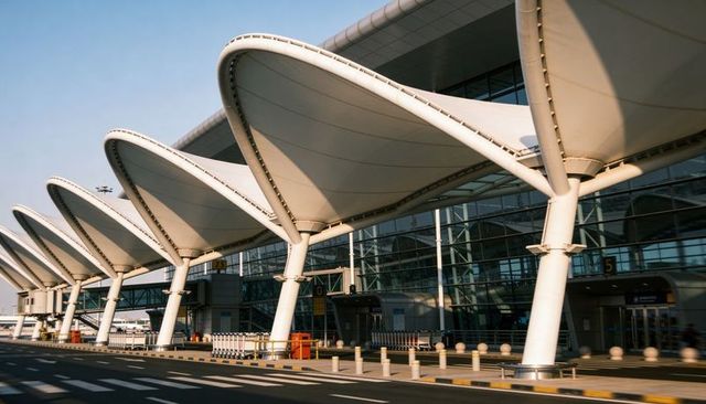 Featuring repeating white canopies and angled columns at airport curbside with glass facade