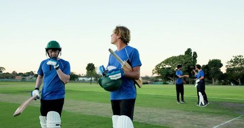 Walking diverse cricket team carrying bats and helmets in blue uniforms leaving pitch