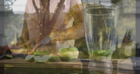 Woman slicing green apples on kitchen counter with blender jar and window reflection