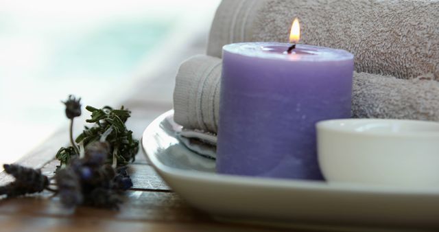 This image portrays a soothing spa scene featuring a lit lavender candle, towels, and lavender flowers on a ceramic plate. Ideal for promoting spa services, wellness retreats, aromatherapy products, and self-care brands.