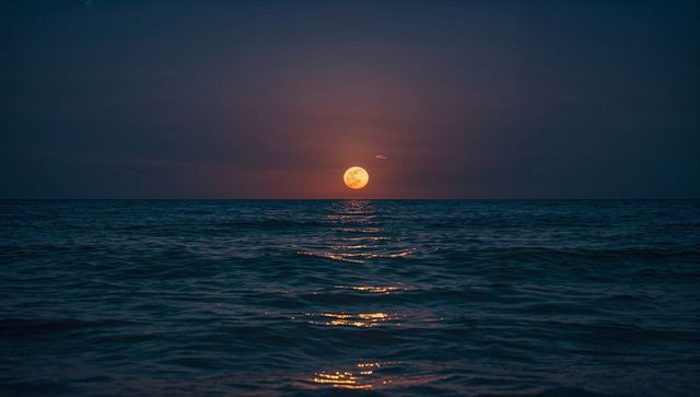 Full moon rising over calm ocean creating golden reflection path to horizon at night