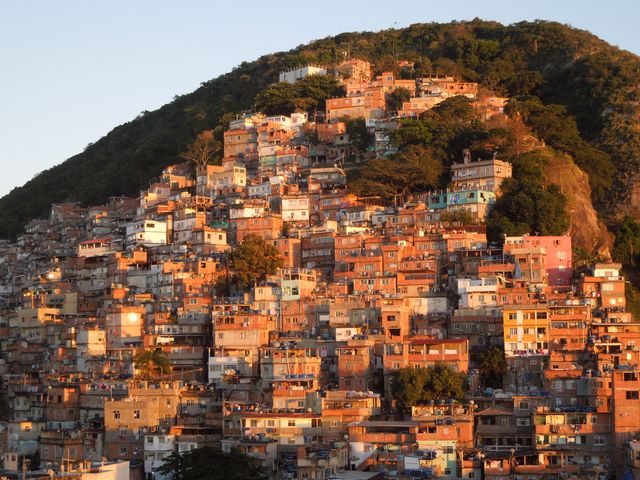 This image showcases a densely populated hillside shantytown with colorful houses. It is an informal urban settlement typical in South America, often representing communities living under the poverty line. Sunlight casts a warm glow on the buildings, enhancing the vibrant hues and providing an atmospheric texture to the setting. Suitable for use in discussions about urban development, socioeconomic challenges, vibrant communities, and travel articles focused on South American regions.