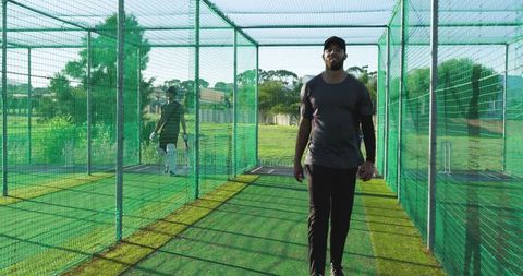 Cricket coach walking down net lane guiding batsman during sunlit outdoor practice session