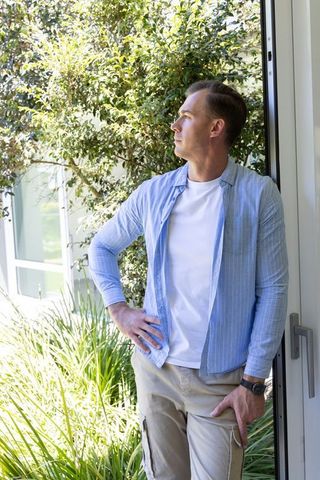 Contemplative man standing in doorway leaning on frame looking toward lush garden