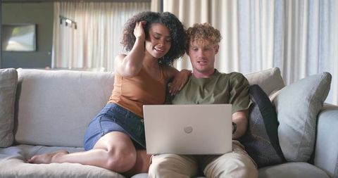 Couple relaxing on sofa sharing laptop, streaming and browsing in minimalist living room