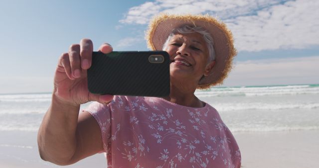 Biracial senior woman taking a selfie with a smartphone at the beach. healthy outdoor leisure time by the sea.