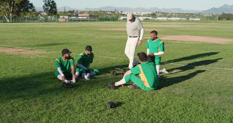 Coach Leading Postgame Talk With Male Baseball Players on Grass Field