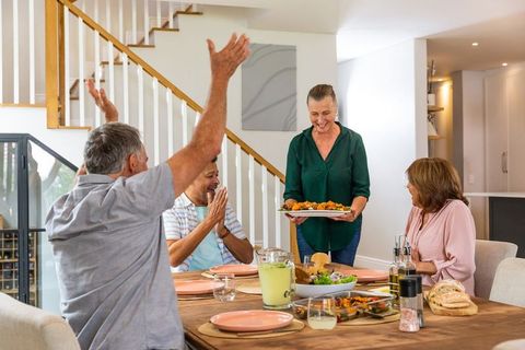Senior Friends Celebrating and Serving Meals at Home Gathering