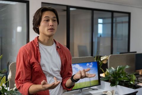 Young professional presenting ideas in modern open-plan office with greenery and monitor