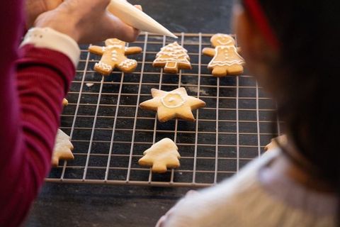 Caregiver decorating gingerbread cookies with child using piping bag on cooling rack