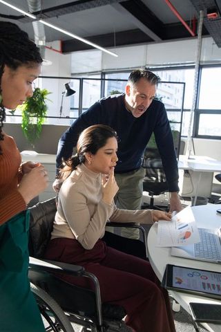 Inclusive team collaborating in modern office while woman in wheelchair analyzing charts